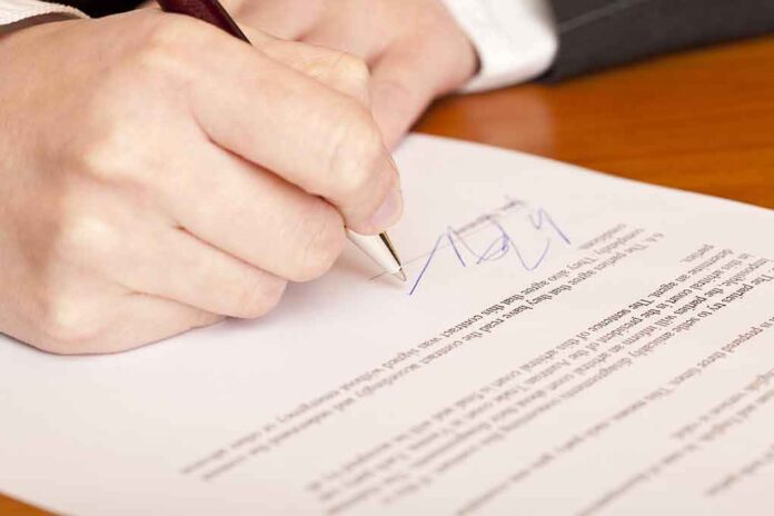 66092728 featured image Hand signing a document on a wooden table