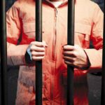 Person in orange jacket behind prison bars