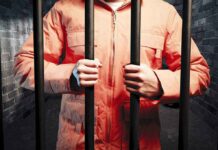 Person in orange jacket behind prison bars