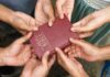 Multiple hands holding a red Bible together
