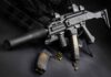 Black assault rifle with silencer and magazine on dark background.