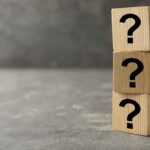 Three wooden blocks with black question marks stacked.
