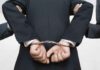 Person handcuffed in suit escorted by two others