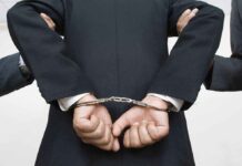 Person handcuffed in suit escorted by two others