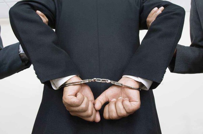 121141399 featured image Person handcuffed in suit escorted by two others