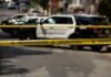 Police tape blocking street with patrol cars