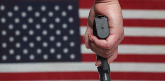 Hand holding gun with American flag background