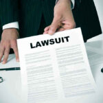 Person holding a document titled "LAWSUIT" in office.