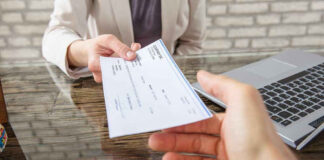Hands exchanging a check near a laptop