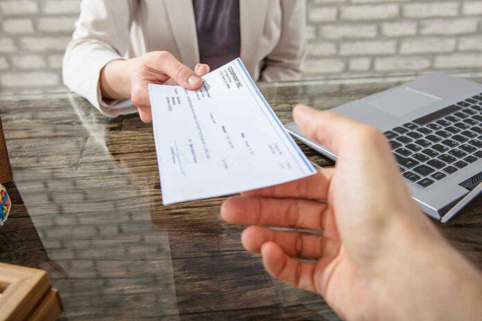 Hands exchanging a check near a laptop