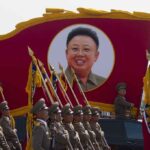 Military parade featuring soldiers and a large banner of Kim Il-sung