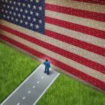 A man in a suit standing in front of a large American flag painted on a wall