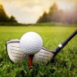 A golf ball on a tee with a golf club resting beside it on green grass