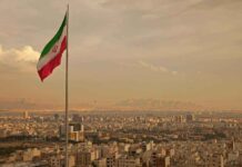 Iranian flag waving over a city skyline with mountains in the background