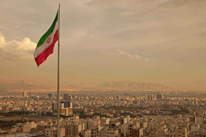 Iranian flag waving over a city skyline with mountains in the background