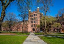 Historic university building surrounded by green grass and trees under a blue sky