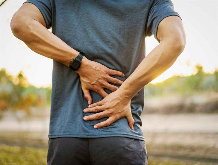Person holding lower back in discomfort outdoors