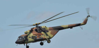 Camouflage military helicopter in flight against blue sky