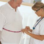 A healthcare professional measuring a patients waist with a tape measure