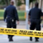 Police officers walking past caution tape at a crime scene