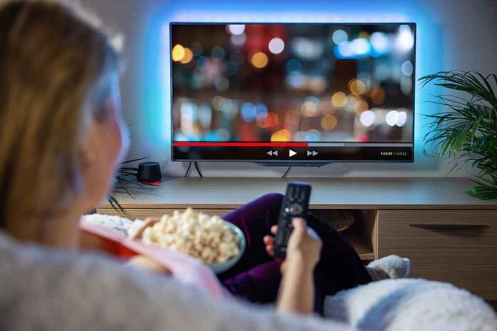 Person sitting on a couch watching a movie on a TV with popcorn in hand