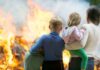 A family watching a large fire outdoors with children in their arms