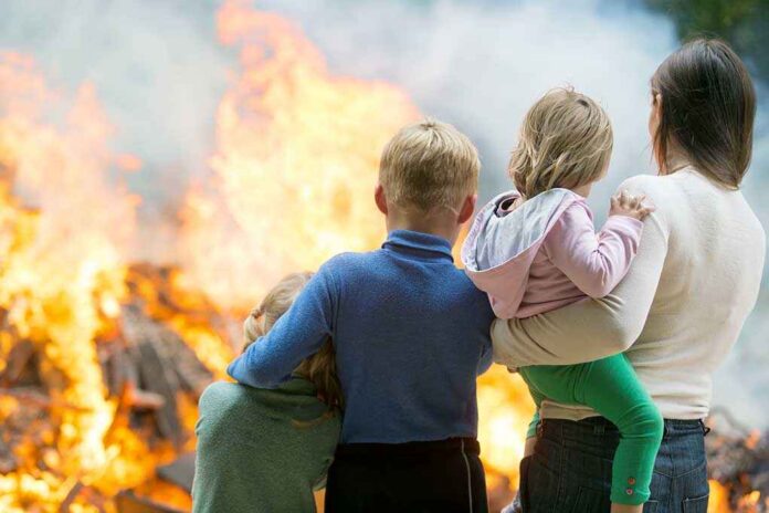 A family watching a large fire outdoors with children in their arms