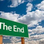 A green road sign displaying the words The End against a cloudy sky