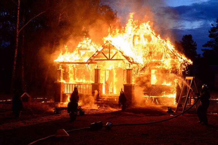 House engulfed in flames with firefighters present.