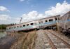 An overturned train on a railway track surrounded by vegetation