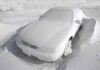 A car completely covered in snow, surrounded by a winter landscape