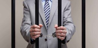 Businessman in a suit holding prison bars with handcuffs on his wrists