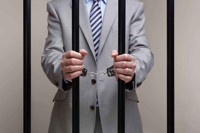 Businessman in a suit holding prison bars with handcuffs on his wrists