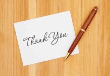 A thank you card with elegant handwriting next to a pen on a wooden table