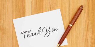A thank you card with elegant handwriting next to a pen on a wooden table