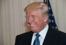 A smiling man in formal attire with an American flag in the background