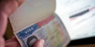 A hand holding an open passport displaying a visa page