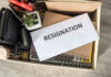 Envelope labeled RESIGNATION atop office supplies in box.