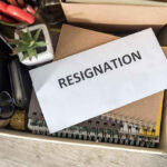 Envelope labeled RESIGNATION atop office supplies in box.