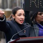 AOC’s Genocide Rant Stuns Munich A woman passionately speaking at a rally with a sign in the background