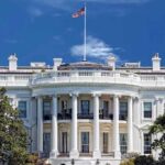 The White House with the American flag flying against a blue sky