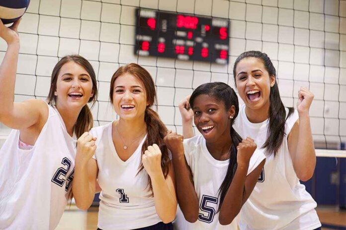 Four female volleyball players celebrating in a gymnasium