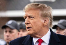 Man in suit and red tie speaking outside.
