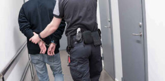 Officer escorting handcuffed person down hallway.