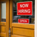 A door with a 'Now Hiring' sign and an 'Open' sign