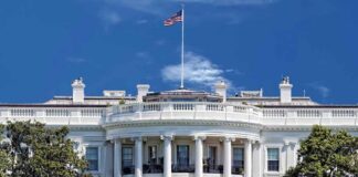 The White House with the American flag flying against a blue sky