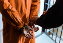 Handcuffed person in orange jumpsuit being escorted.
