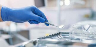 Gloved hand holding a dental mirror over instrument tray