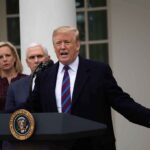 man speaking at podium with officials standing behind