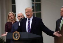 man speaking at podium with officials standing behind